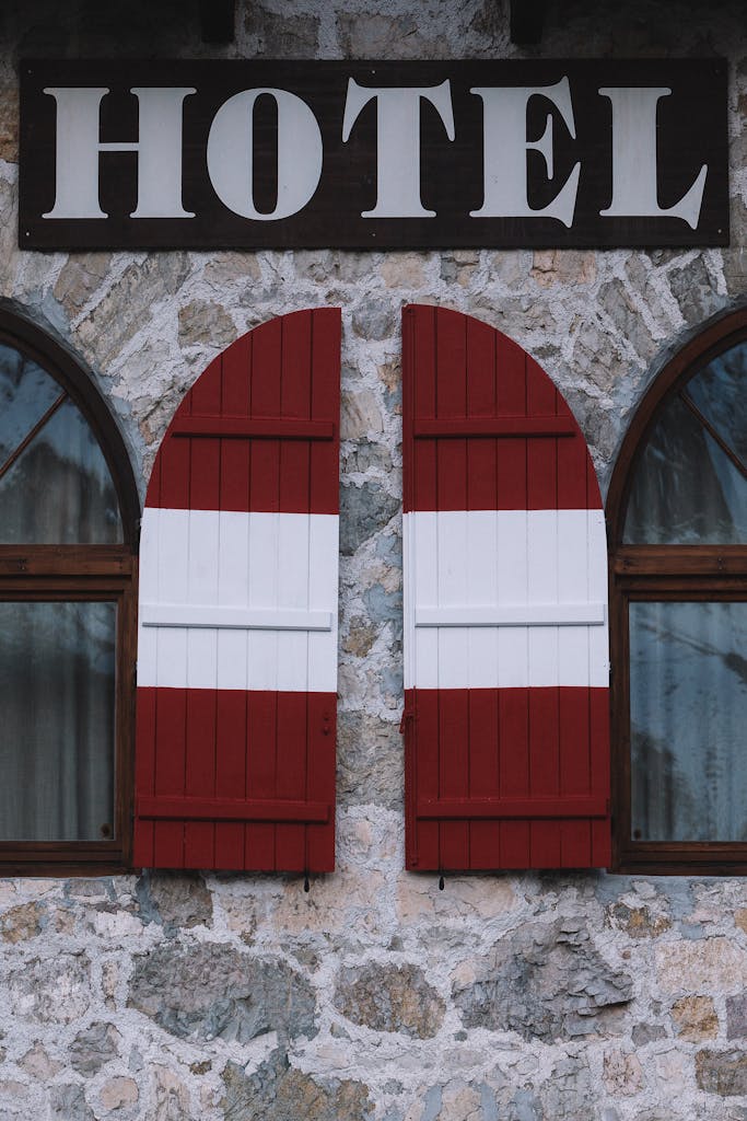 Close-up of a stone hotel facade with red and white wooden shutters, creating a cozy and inviting atmosphere.