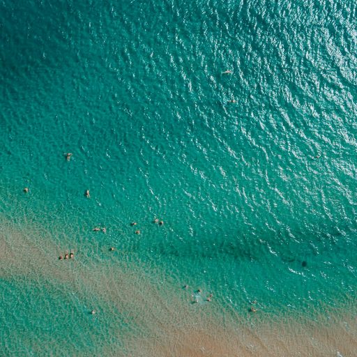 Drone shot capturing the vibrant blue waters and swimmers at a Greek beach.