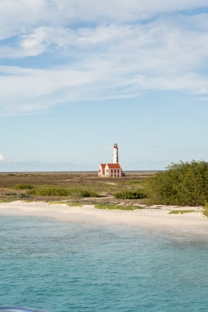 Serene view of Klein Curaçao island's lighthouse and sandy beach under a blue sky.
